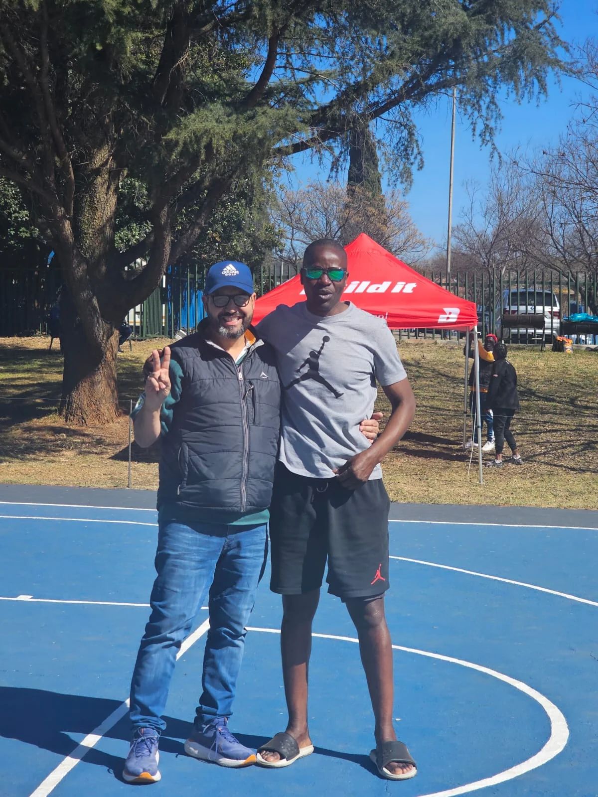 Two people pose together on the blue outdoor basketball court