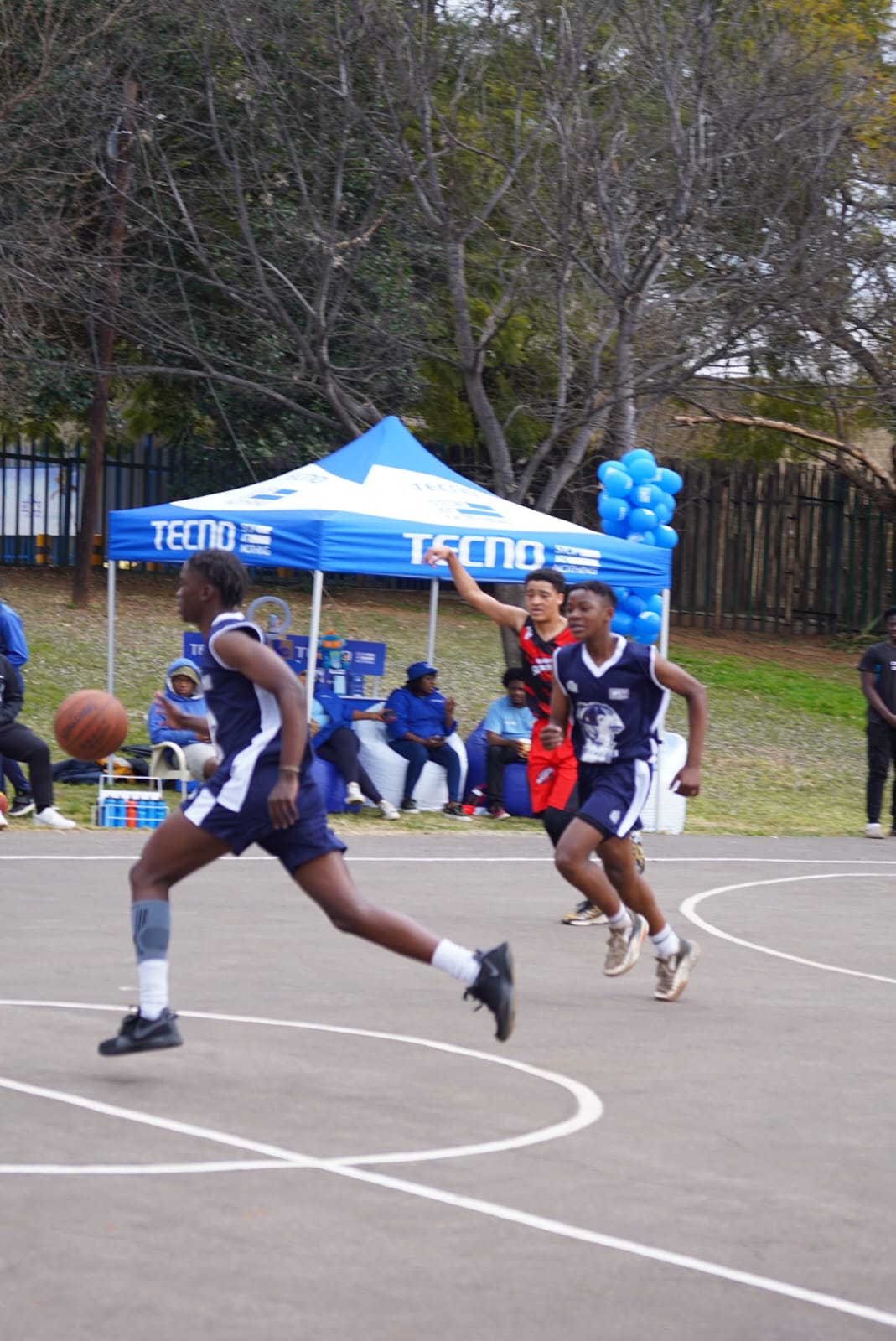 Three basketball players sprint up the outdoor court